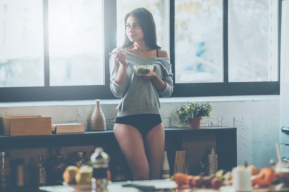 Młoda kobieta je śniadanie i zastanawia się, co jeść, żeby schudnąć.